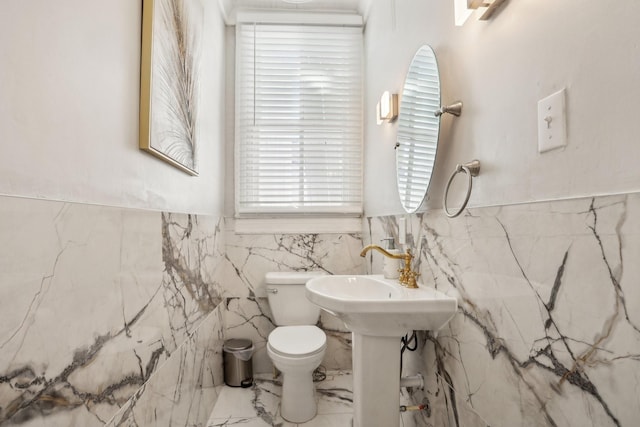 bathroom featuring marble finish floor, a wainscoted wall, tile walls, and toilet