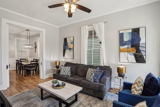 living room with baseboards, ornamental molding, wood finished floors, and ceiling fan with notable chandelier