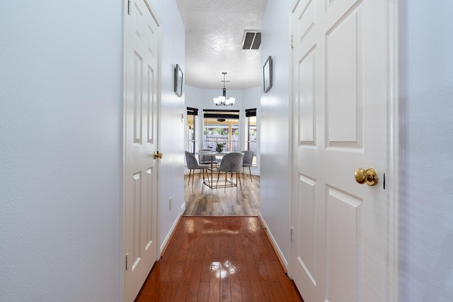 hallway with an inviting chandelier, dark wood-type flooring, and a textured ceiling