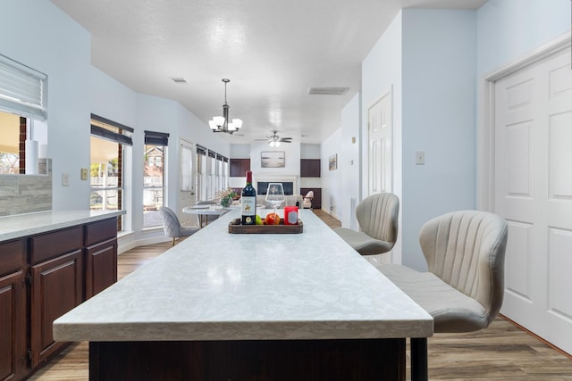 kitchen with pendant lighting, a kitchen breakfast bar, a center island, light hardwood / wood-style floors, and dark brown cabinets