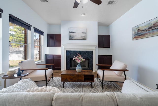 living room with ceiling fan, a high end fireplace, and light hardwood / wood-style floors