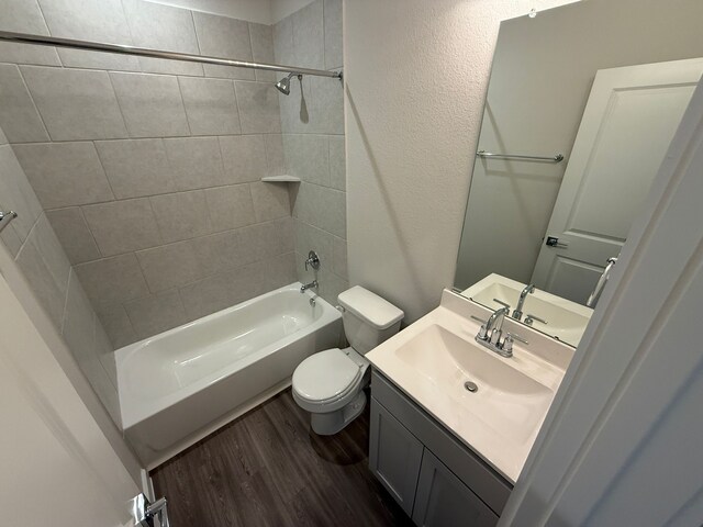 full bathroom with hardwood / wood-style flooring, tiled shower / bath, vanity, and toilet