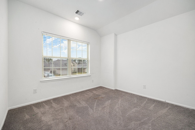 spare room featuring vaulted ceiling and dark colored carpet