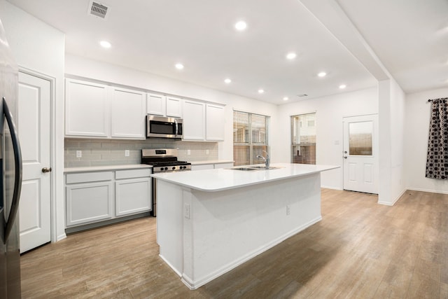 kitchen with appliances with stainless steel finishes, tasteful backsplash, an island with sink, white cabinetry, and sink