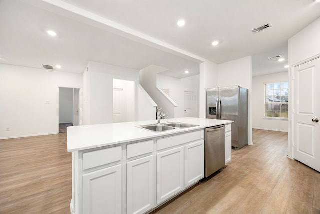 kitchen featuring sink, white cabinetry, light wood-type flooring, stainless steel appliances, and a kitchen island with sink