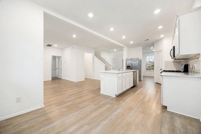 kitchen featuring appliances with stainless steel finishes, white cabinetry, decorative backsplash, a center island with sink, and light hardwood / wood-style flooring