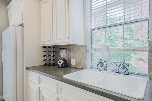 kitchen featuring decorative backsplash, white cabinets, dark countertops, freestanding refrigerator, and a sink