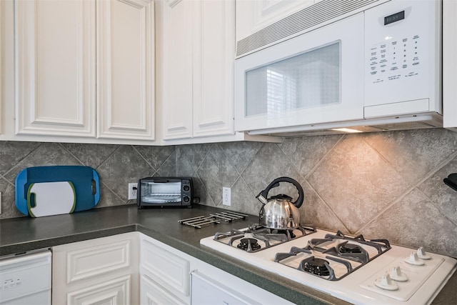 kitchen with white appliances, dark countertops, and white cabinetry