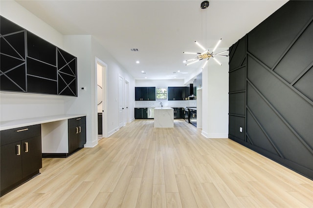 unfurnished living room featuring an inviting chandelier, sink, and light hardwood / wood-style floors