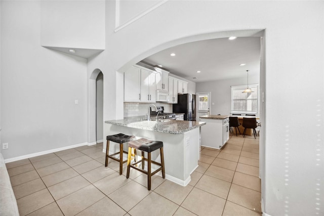 kitchen with light tile patterned flooring, white cabinetry, a center island, black refrigerator, and kitchen peninsula