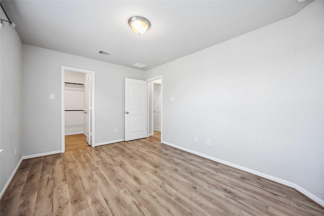 unfurnished bedroom featuring a walk in closet, a closet, and light wood-type flooring