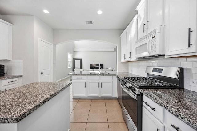 kitchen with light tile patterned floors, stainless steel gas stove, white cabinetry, backsplash, and dark stone counters