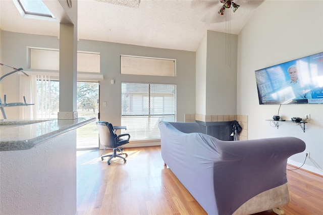 living area with high vaulted ceiling, light wood finished floors, baseboards, and a textured ceiling