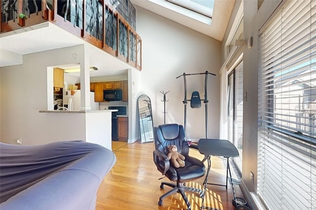 bedroom featuring light wood-type flooring, a skylight, high vaulted ceiling, and refrigerator with ice dispenser