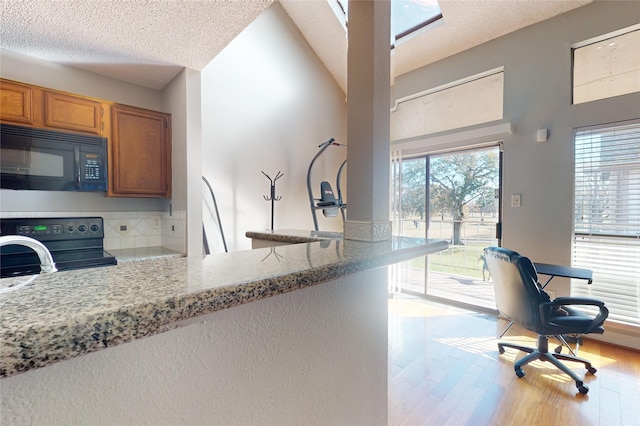 kitchen with black appliances, light stone counters, kitchen peninsula, a textured ceiling, and light wood-type flooring