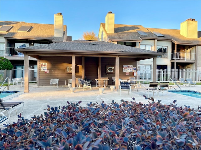 back of house featuring roof with shingles, fence, and a community pool