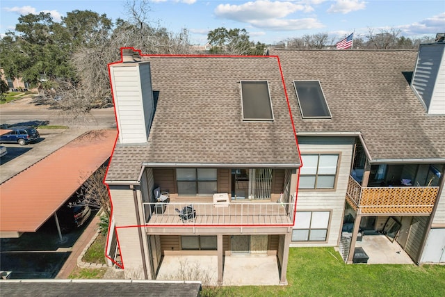 rear view of house featuring roof with shingles, a chimney, a patio, and a balcony