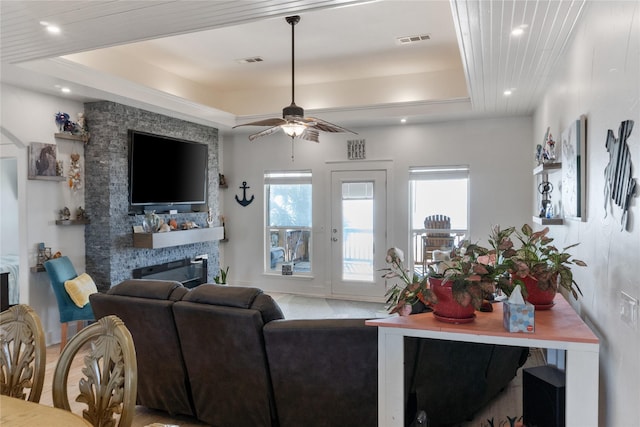 living room with ceiling fan, a stone fireplace, and a raised ceiling