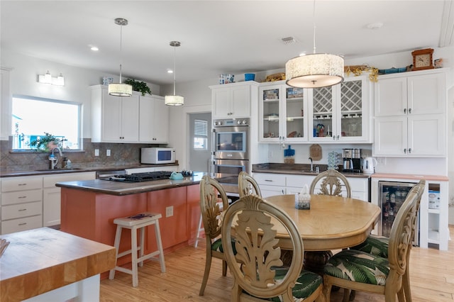 kitchen featuring double oven, wine cooler, white cabinets, hanging light fixtures, and a center island