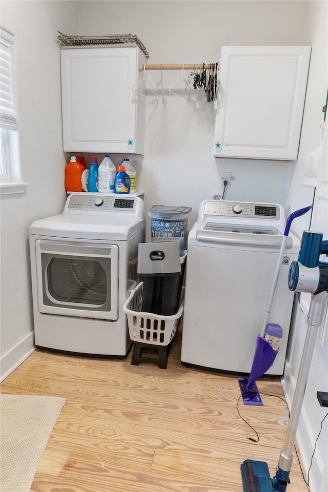 clothes washing area with cabinets, washer and dryer, and light wood-type flooring