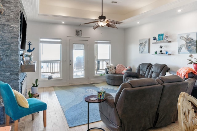 living room with a raised ceiling, ceiling fan, a healthy amount of sunlight, and light wood-type flooring