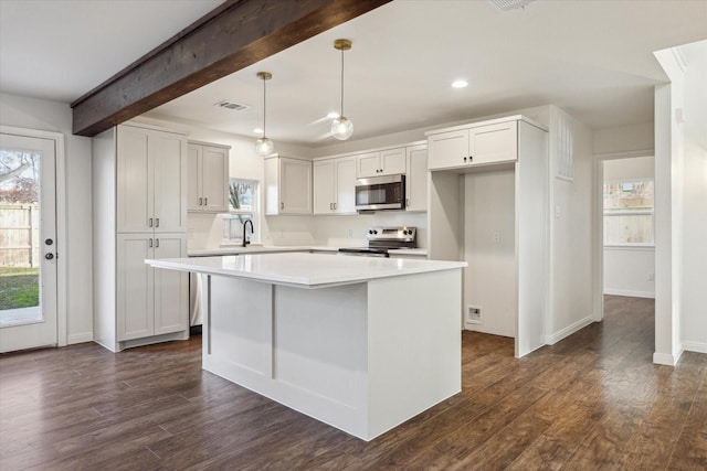 kitchen featuring stainless steel appliances, white cabinetry, hanging light fixtures, and a center island