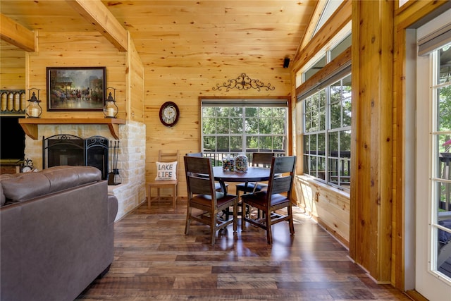 dining area featuring a stone fireplace, dark wood-type flooring, lofted ceiling with beams, and wood walls