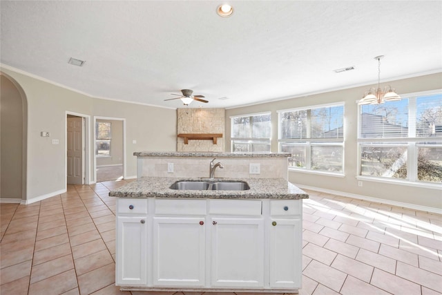 kitchen with light tile patterned flooring, decorative light fixtures, an island with sink, sink, and white cabinets