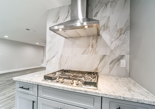 kitchen featuring extractor fan, light stone counters, gray cabinets, stainless steel gas stovetop, and decorative backsplash