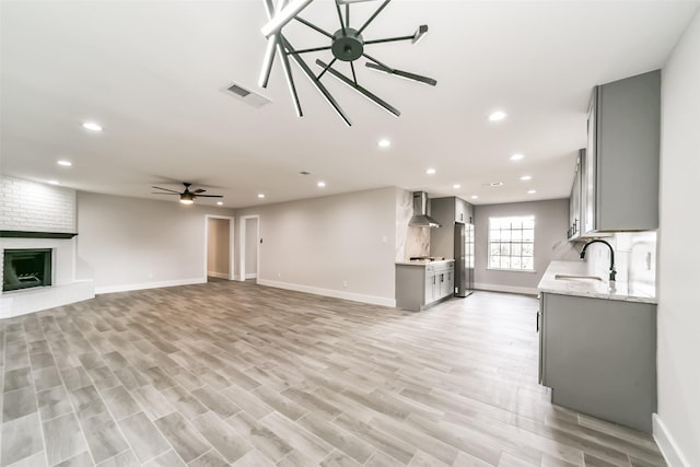 unfurnished living room featuring ceiling fan, a fireplace, sink, and light hardwood / wood-style flooring