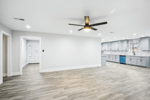 unfurnished living room featuring ceiling fan, a healthy amount of sunlight, sink, and light wood-type flooring