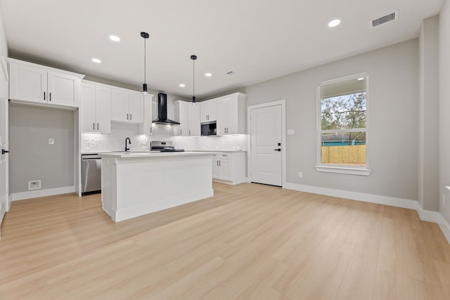 kitchen featuring white cabinets, decorative backsplash, hanging light fixtures, a center island, and wall chimney exhaust hood