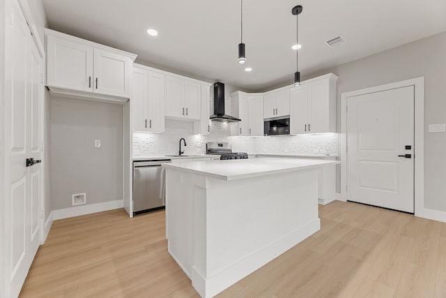 kitchen with decorative light fixtures, white cabinetry, a center island, stainless steel appliances, and wall chimney range hood