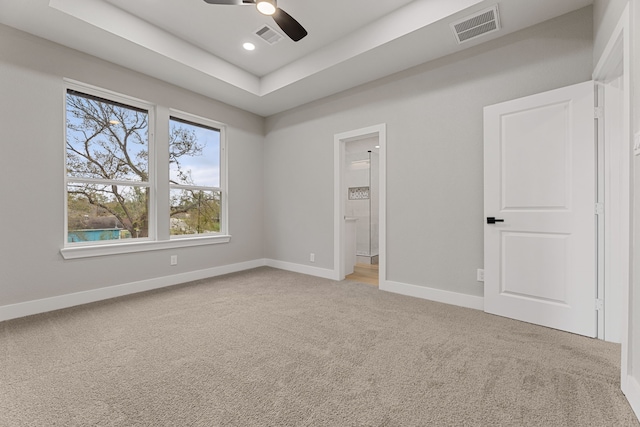 unfurnished bedroom with ceiling fan, ensuite bath, a tray ceiling, and carpet floors