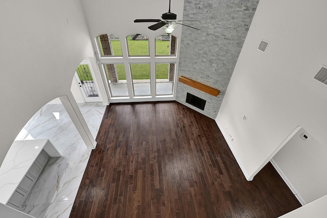 unfurnished living room featuring a high ceiling, ceiling fan, hardwood / wood-style flooring, and a fireplace