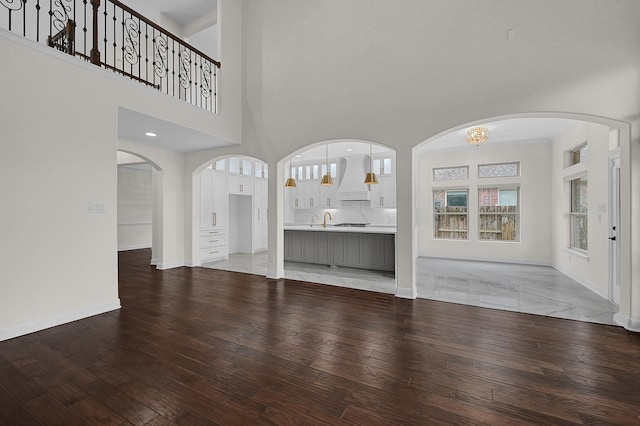 unfurnished living room with sink, hardwood / wood-style flooring, and a towering ceiling