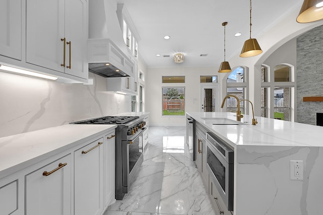 kitchen with white cabinetry, hanging light fixtures, a center island with sink, custom range hood, and stainless steel appliances