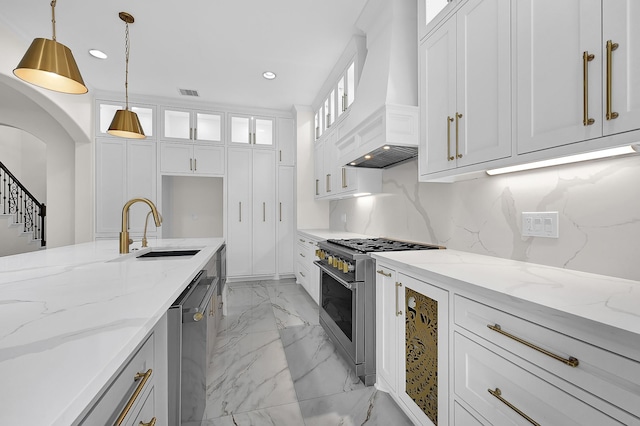 kitchen with premium range hood, appliances with stainless steel finishes, decorative light fixtures, white cabinetry, and sink