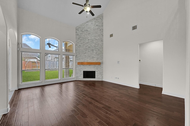 unfurnished living room featuring ceiling fan, dark hardwood / wood-style floors, high vaulted ceiling, and a stone fireplace