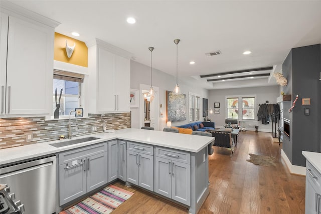 kitchen with a peninsula, a sink, open floor plan, light countertops, and dishwasher