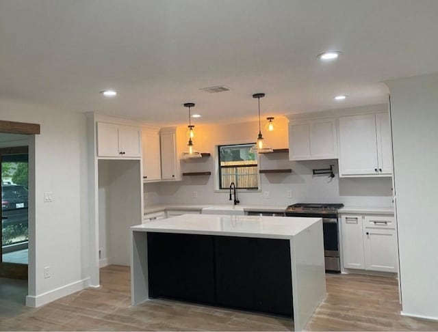 kitchen with sink, stainless steel gas range oven, a center island, pendant lighting, and white cabinets