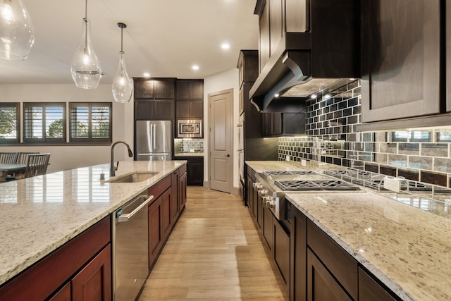 kitchen featuring sink, backsplash, hanging light fixtures, light stone counters, and stainless steel appliances