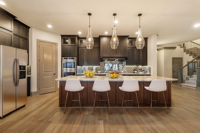 kitchen featuring stainless steel appliances, pendant lighting, light stone counters, and a spacious island