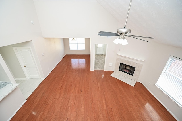 unfurnished living room with ceiling fan, wood-type flooring, high vaulted ceiling, and a tile fireplace