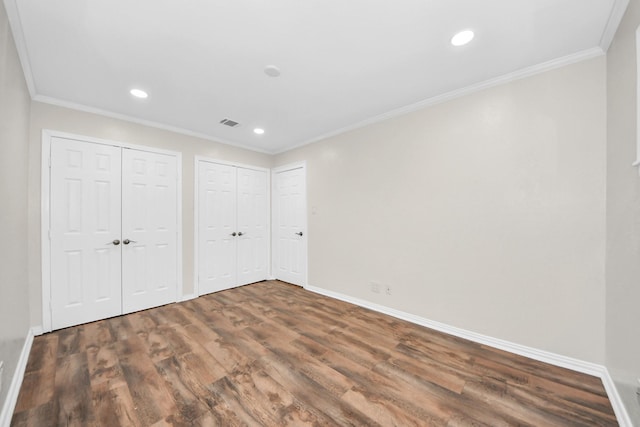 unfurnished bedroom with crown molding, dark wood-type flooring, and two closets