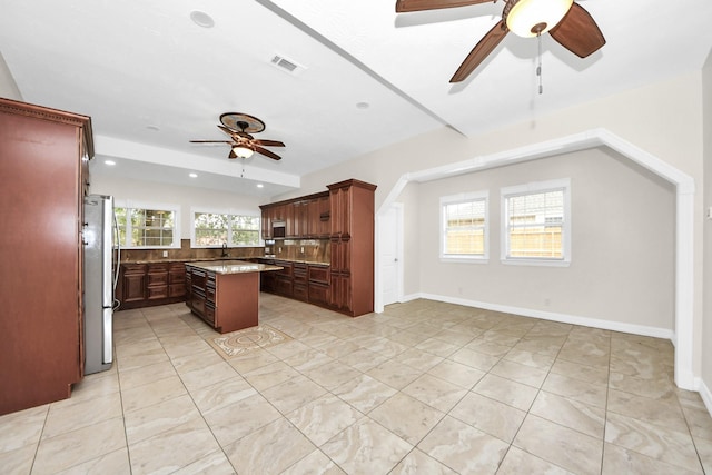 kitchen with light tile patterned floors, ceiling fan, appliances with stainless steel finishes, tasteful backsplash, and a kitchen island