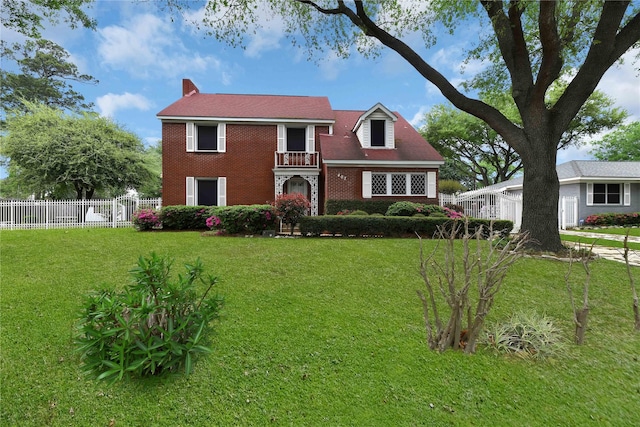 view of front of property featuring brick siding, a front yard, fence, and a balcony