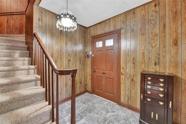 foyer entrance with baseboards, stairway, wood walls, and an inviting chandelier