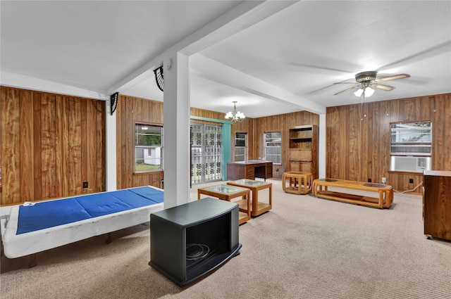 carpeted living room with ceiling fan with notable chandelier, wood walls, plenty of natural light, and beam ceiling