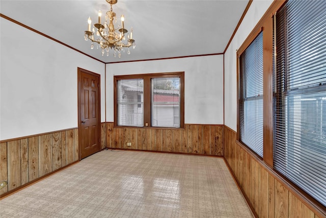 spare room with wood walls, a wainscoted wall, a chandelier, and crown molding
